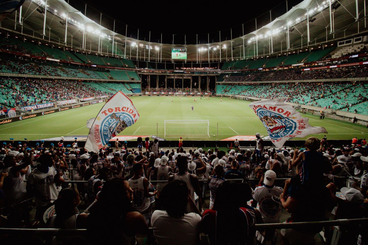 gallery-1 Energetic soccer fans cheer during a night match at a large stadium, creating an exciting atmosphere.
