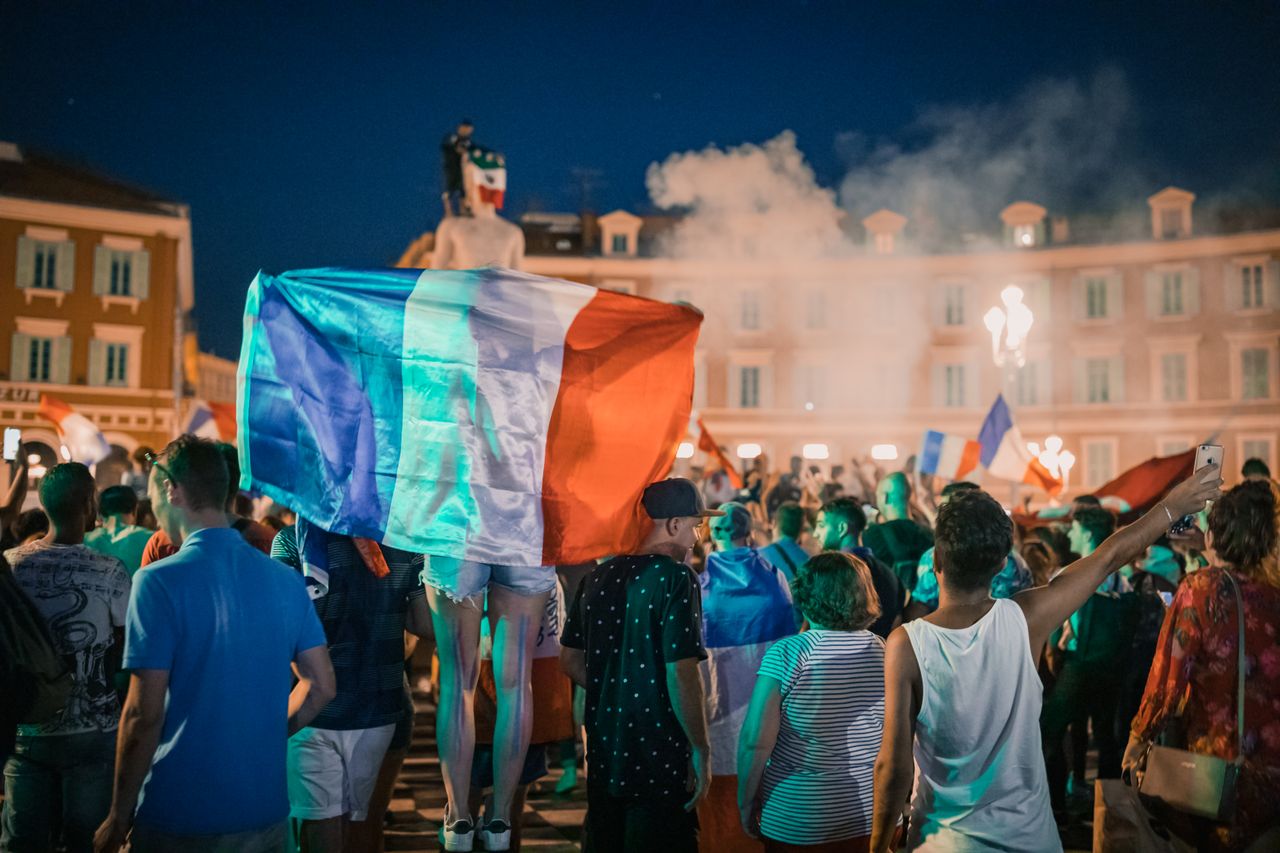 services-img Vivid night-time celebration in France with crowds waving flags in city square.